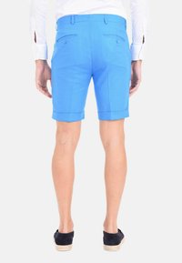 Pantaloni corti blu brillante con una vestibilità su misura, con risvolti, tasche posteriori e una texture liscia. Indossati con una camicia bianca a maniche lunghe.