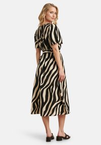 Zwart en beige zebra-gestreepte midi-jurk met korte mouwen, stoffen riem in de taille en een vloeiende rok. Draagt met zwarte hoge hakken sandalen.