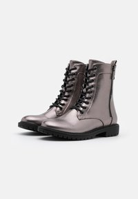 Botas de tobillo plateadas metálicas con cordones negros, punteras redondas y cremalleras laterales. Suelas de goma resistentes ofrecen tracción y durabilidad.