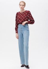 Bordeaux polka dot blouse met lange geplooide mouwen, gecombineerd met hoge lichtblauwe rechte jeans en donker gekleurde enkellaarzen met hak.