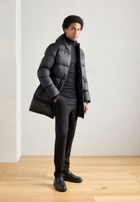 Crna puf jakna s kapuljačom; glatka, sjajna tkanina; uparena s crnim rolkom i uskim hlačama; crni mokasini upotpunjuju look.