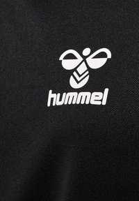 Tessuto nero con una superficie texture presenta un logo stampato bianco di un'ape stilizzata e il nome del marchio "hummel" sottostante.