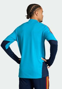 Vaaleansininen urheilupaita laivastonsinisillä hihoilla ja sivupaneeleilla; siinä on korkea kaulus ja tekstuurilliset kuviot hihoissa.