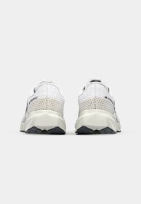 Running shoes in white and light gray with a textured mesh upper, angular sole design, and contrasting black accents.