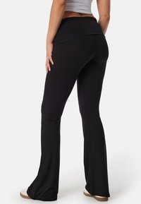 Zwarte uitlopende broek gemaakt van rekbaar materiaal, met een hoge tailleband. Gladde textuur met een aansluitende pasvorm en uitlopende zoom.