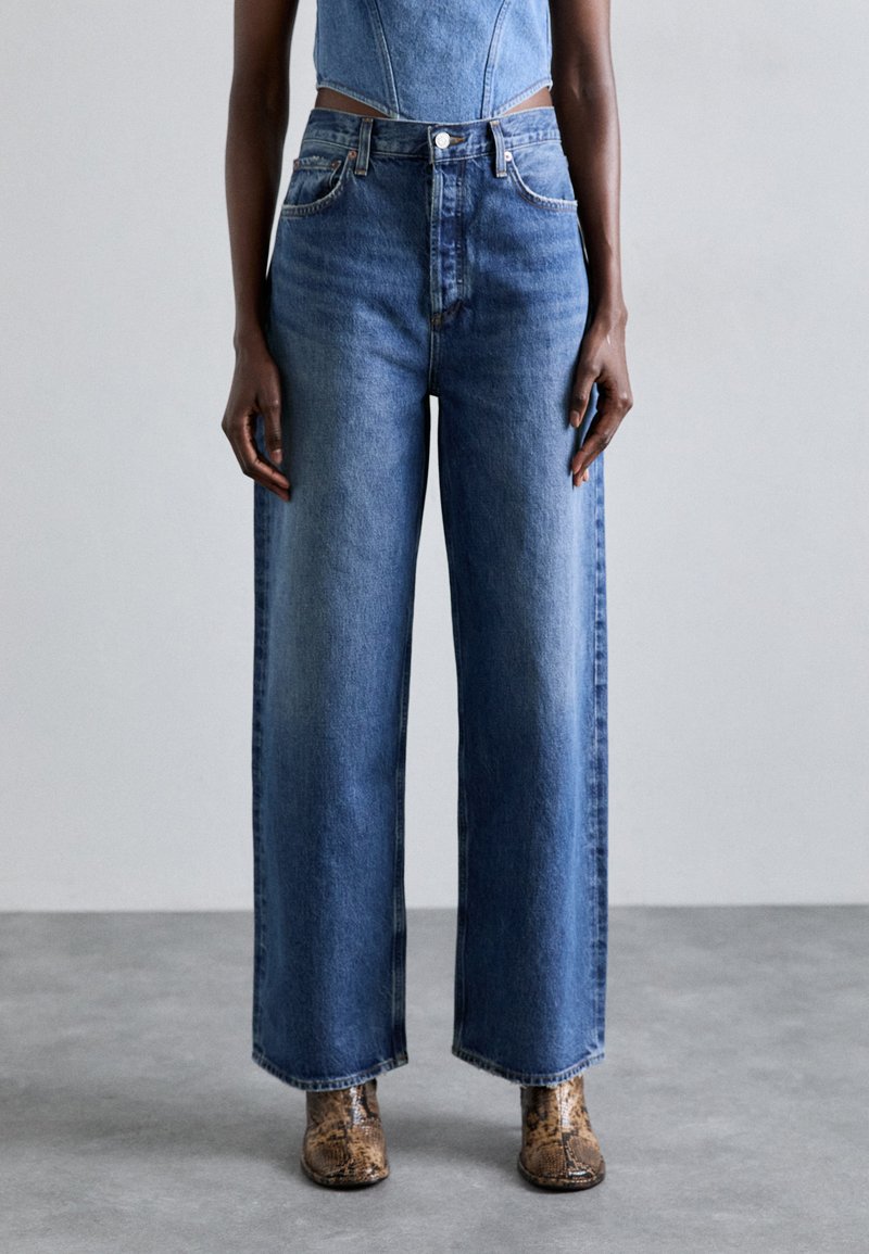 Wide-leg blue denim jeans with a high waist, faded wash, and subtle stitching details. Paired with textured brown ankle boots.