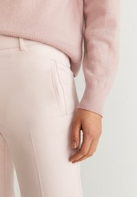 Světle růžový svetr s žebrovanými manžetami, kombinovaný se světlými růžovými kalhotami na míru, které mají boční kapsy a hladkou texturu.