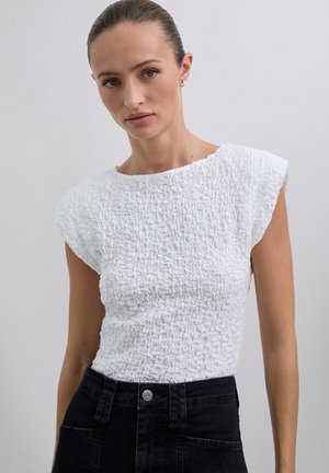 Top blanco texturizado con escote redondo y mangas cortas. Presenta un diseño arrugado y se combina con pantalones negros de talle alto.