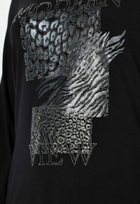 Czarny top z długim rękawem z metalicznym srebrnym wzorem zwierzęcym i teksturowanymi wzorami. Ozdobiony cyrkoniami i geometrycznymi kształtami.