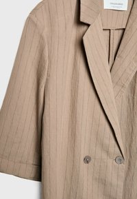 Blazer de lino marrón claro con sutiles rayas. Presenta un cuello con muescas, botones dobles y mangas cortas. Textura suave.