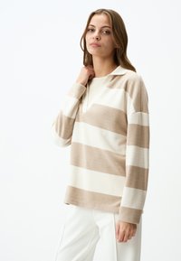 Pullover a maniche lunghe a righe beige e crema con colletto. Morbido al tatto, vestibilità comoda e scollo a V. Sfondo semplice.