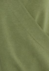 Telaje de algodón verde con una textura suave, que presenta ligeras variaciones en el tono y sutiles detalles de costura, creando una apariencia en capas.
