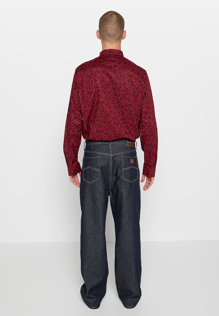 Rotes Langarmhemd mit schwarzem abstraktem Muster, kombiniert mit dunkelblauen Jeans. Die Jeans verfügen über fünf Taschen und einem braunen Lederdetail auf der Rückseite.