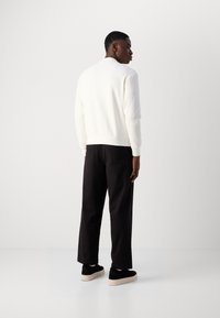 Sudadera blanca de punto texturizado con puños y dobladillo de canalé, combinada con pantalones negros de pierna ancha y zapatos negros de mocasín con suela beige.