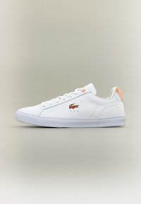 White tennis shoes with a smooth leather upper, flat rubber sole, tonal laces, and a subtle orange accent on the heel and logo.