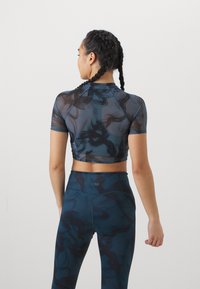 Top court à manches courtes en matériau transparent bleu foncé avec des tourbillons abstraits, associé à un legging taille haute présentant un motif similaire.