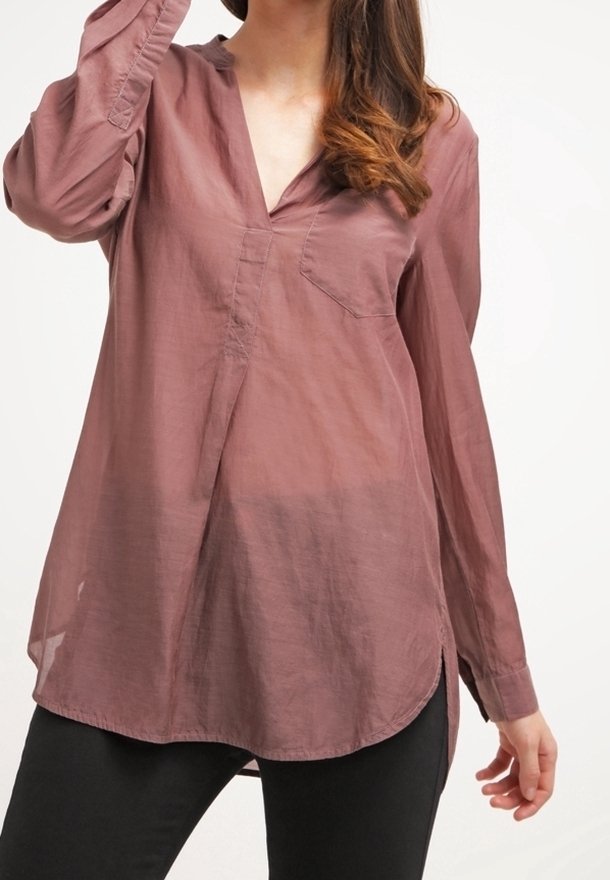 Chemise mauve à manches longues en tissu léger, avec un col en V, une poche poitrine et des fentes sur les côtés de l'ourlet pour plus de détails.