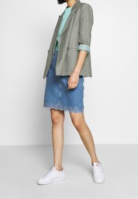 Šedý kostkovaný blazer, svetle modrá košile, džíny sukně se vykrojeným okrajem a bílé tenisky. Moderní, casual outfit s vrstvenými texturami.