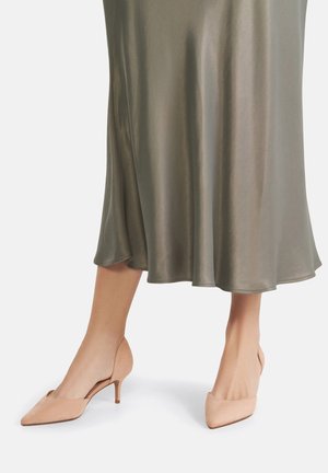 Untere Beine mit beigefarbenen Wildleder-Kitten-Heels mit spitzer Zehenpartie, kombiniert mit einem fließenden, olivgrünen Satin-Midirock.