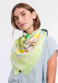 Foulard di seta colorato con una base verde, illustrato con un design di uccello e cuore, rifinito con una forma triangolare e una texture morbida.