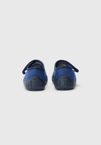 Tumši zilas slip-on kurpes ar mīkstu auduma augšdaļu, biezu gumijas zoli un nelielu Velcro siksnu drošai pieguļošanai, ar faktūru uz zoles.