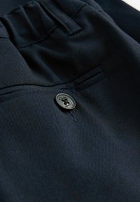 Pantaloni blu scuro realizzati in tessuto testurizzato, dotati di una tasca frontale e un bottone rotondo nero con incisione "Clarks".