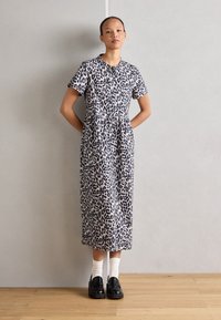 Midi šaty s leopardím printom, krátkymi rukávmi, okrúhlym výstrihom, priliehavým pásom a rozšíreným lemom. Čierne topánky a biele ponožky dopĺňajú tento vzhľad.