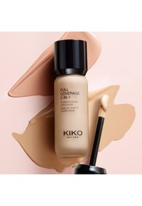 Flacon de fond de teint et correcteur 2-en-1 Full Coverage de KIKO Milano avec applicateur, posé sur des échantillons de maquillage beige et brun estompés.