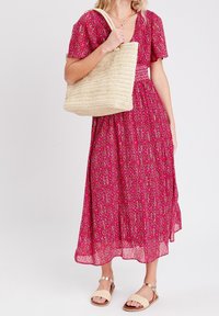 Robe maxi florale rose avec des manches courtes et un décolleté en V. Accompagnée d'un sac tote tissé beige et de sandales légères.