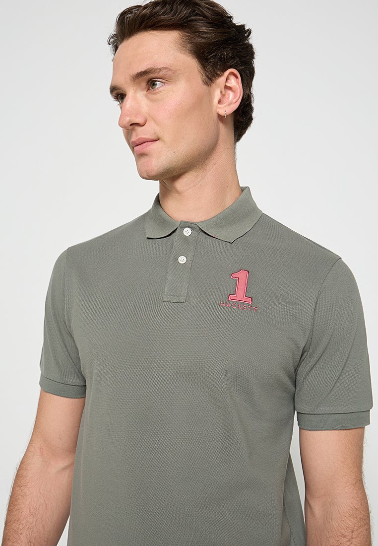 Green polo shirt in breathable fabric, featuring a pointed collar, two button placket, and a pink embroidered number '1' on the chest.