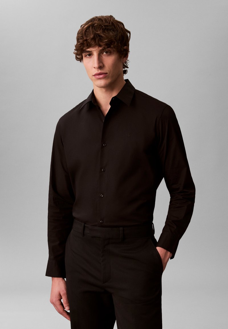 Black long-sleeve shirt with a button-down collar, made of smooth fabric, featuring subtle logo embroidery and a tailored fit.