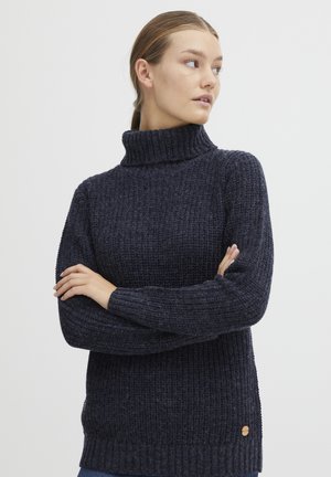 Mørkeblå turtleneck genser med teksturert strikkemønster, ribbestrikkede mansjetter og kant, med en liten trelogo-akse på venstre side.