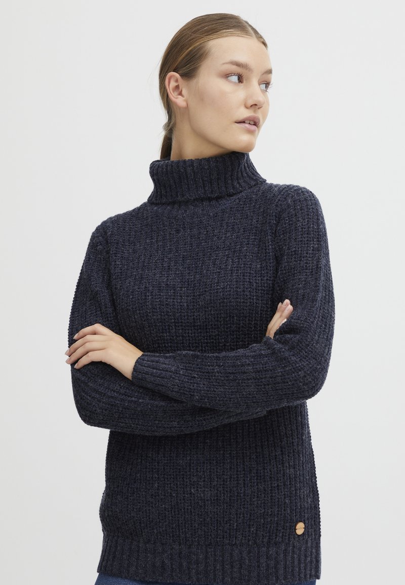 Navy blue turtleneck sweater with a textured knit pattern, ribbed cuffs, and hem, featuring a small wooden logo accent on the left side.