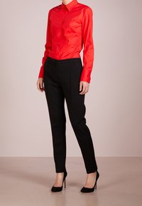 Rode overhemdd blouse met een kraag en lange mouwen, gecombineerd met zwarte op maat gemaakte broeken en zwarte hoge hakken.