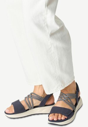 Sandales navy avec un design de bride entrecroisée texturé, un bon soutien du talon et une semelle légère couleur crème. Portées avec un pantalon blanc ample.