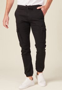 Zwarte cargo joggers met elastische boorden, een trekkoord in de taille en meerdere zijzakken. Gemaakt van een katoenmix met een gladde textuur.