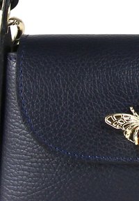 Marineblauwe leren handtas met een gestructureerd oppervlak, gouden vlinderaccent en contrasterende stiksels langs de klepafsluiting.