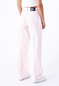 Ljusrosa vida jeans med hög midja, med en svart märkesetikett på baksidan och två fackfickor. Mjuk, slät textur.