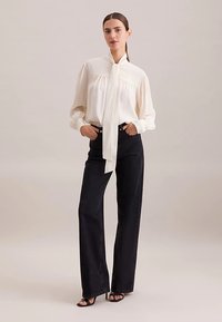 Hvid silke skjorte med spids krave og langt bindebånd, kombineret med højtaljede sorte jeans med vide ben. Glat tekstur, få detaljer.