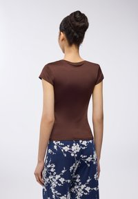 T-shirt marrone aderente con maniche corte e scollo rotondo, abbinato a pantaloni navy con fantasia che presenta motivi floreali bianchi.