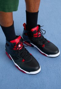 Černé a červené vysoké sportovní boty s hladkým koženým svrškem, kontrastními akcenty a bílou gumovou podrážkou, šněrováním a texturovanými detaily.