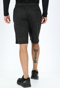 Zwarte sportshorts van textiel, met een elastische tailleband, zijzakken en een subtiel gedrukt logo op het onderbeen.