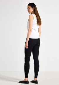 Vit ribbad linne i kombination med svarta leggings. Linnet har breda axelremmar och en figursydd passform. Leggingsen är smala och når anklarna.
