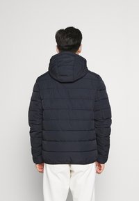 Marineblaue Steppjacke mit Kapuze, mit horizontalen Nähten und strukturierter Oberfläche. Vorderer Reißverschluss und elastische Bündchen.