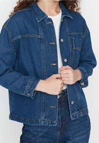 Sininen farkkutakki, jossa on klassinen kaulus, etupainikkeet ja rintatasku. Kangas on tekstuuripintainen ja hieman oversized.