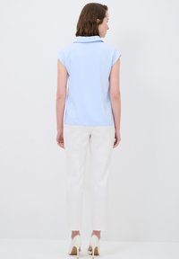 Blusa azzurro chiaro con colletto, maniche a cappuccio corte, abbinata a pantaloni bianchi slim-fit e scarpe con tacco alto bianche. Tessuto morbido.