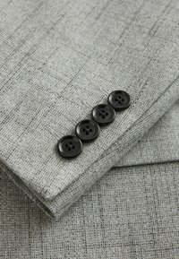 Manche de costume gris texturé avec quatre boutons noirs alignés près du poignet.