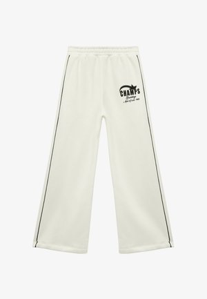Pantalones de chándal blancos con un logo negro de "CHAMPS", cinturilla elástica y detalle de piping negro en los laterales; tejido suave y texturizado.