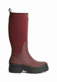 Hög, vinröd gummiboot med en texturerad svart sula. Har ett slätt skaft, förstärkt tå och en tygdragrem på baksidan.