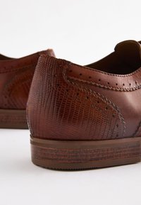 Chaussures en cuir marron présentant une finition texturée avec un motif reptile, des détails perforés et une semelle en caoutchouc profilée basse.